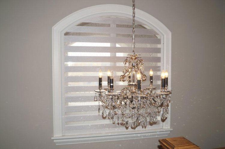 An arched window with white shutters behind a chandelier.